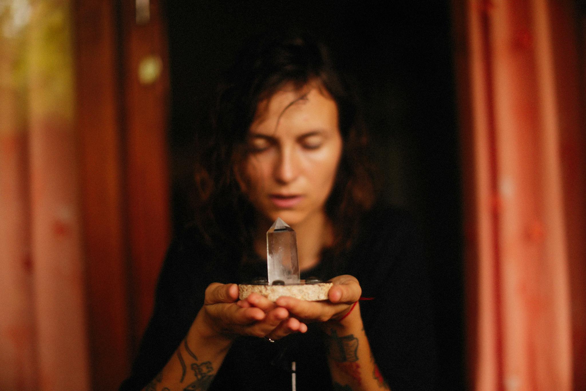 A woman meditates with a healing crystal held in her hands inside a warm, cozy room.